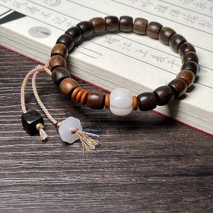 Macro detail of dark brown agarwood prayer beads with white pumpkin charm and tassels