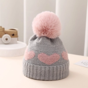 Detail of grey knitted baby hat with pink heart jacquard and soft faux fur pom-pom