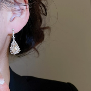 Nahaufnahme eleganter goldener Tropfenohrringe mit Kristallen an einem Modell getragen