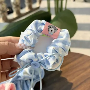Detail of blue plaid scrunchie featuring a cartoon dog label and sky blue button charm