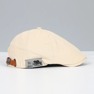 Detail of beige canvas beret featuring a brown leather buckle and embroidered side label
