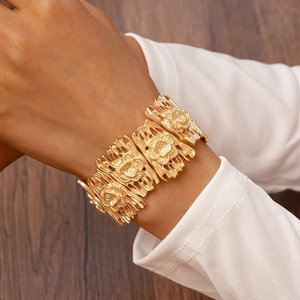 Detailed view of wide matte gold镂空 floral pattern bangle on a female model's wrist
