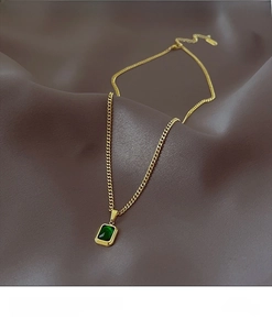Detail of vintage gold necklace with emerald pendant on textured leather background