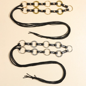Detail of black faux leather belts with gold and silver metal rings and tassel ends