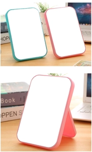 Detail showing foldable portable makeup mirrors in pink and blue on a wooden desk