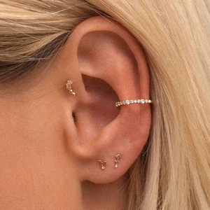 Macro shot of gold ear cuff and stud earrings set with sparkling stones on a model ear