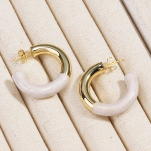 Détail macro de boucles d'oreilles en C dorées avec incrustation en résine marbrée