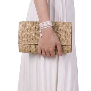 Detail of hand-held straw woven clutch bag with elegant bead bracelet on white background