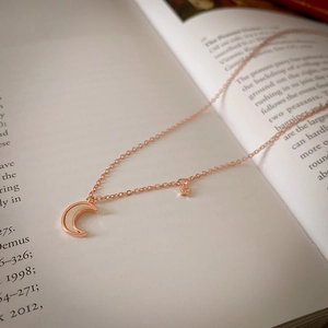Détail du collier à pendentifs lune et étoile en or rose sur un livre ouvert