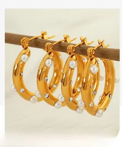 Close-up of gold C-shaped earrings with white pearls and crystals on a wooden branch