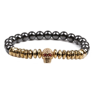 Black hematite beads bracelet with golden skull charm and red eyes on white backdrop