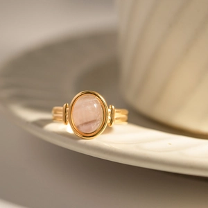 Detail of oval pink quartz ring with ribbed gold band on a white ceramic tray