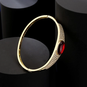 Luxurious open gold bangle with large red oval gemstone and pavé-set zircons on black stand