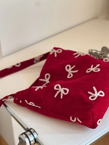 Detailed view of red corduroy shoulder bag with white bow embroidery texture