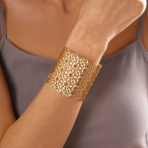 Dettaglio di un ampio bracciale a polsino dorato traforato con motivi floreali a pizzo