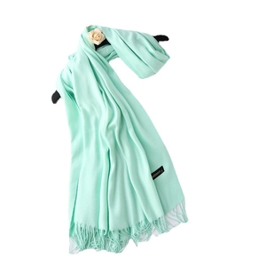 Mint green cashmere scarf with tassel hem hanging on a hanger with a beige rose
