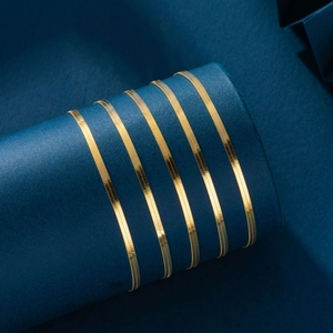 Macro shot of a golden s925 sterling silver flat snake chain on a navy blue stand