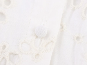 Detail shot of white eyelet embroidery dress featuring fabric-covered button and lace texture