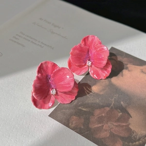 Macro detail of 3D rose petal earrings with pink gradient and crystal center on a book