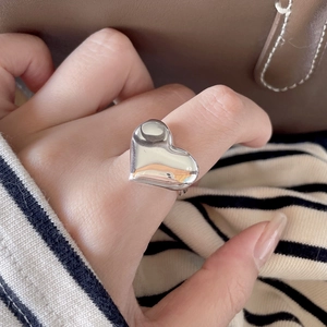 Close-up of a large polished silver heart ring worn on a hand with casual knitwear
