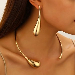 Set orecchini a goccia e collana rigida in oro lucido dal design fluido e minimalista
