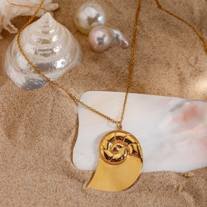 Detailed close-up of a golden nautilus shell pendant necklace on a sandy beach