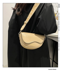 Close-up of beige saddle bag with textured wide strap worn by a model in a minimal setting
