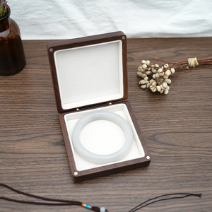 Macro detail of a dark wood jewelry box with a white jade bangle on soft lining