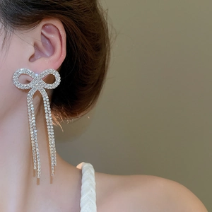 Close-up of sparkling bow tassel earrings with crystals worn by a model in soft light