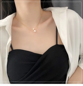 Close-up of a double-layered gold necklace with two white pearl pendants on neck