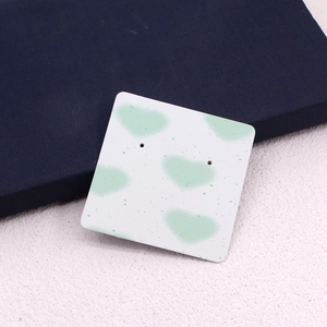 Detail of square paper earring display card with green heart pattern and pre-punched holes