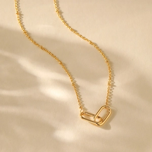 Detail of 18K gold plated fan chain with interlocking oval clasp on a textured surface