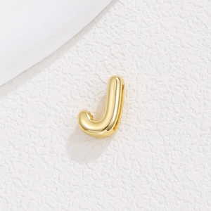 Close-up of a 18K gold plated bubble letter J pendant on a textured white stone surface