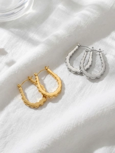 Macro shot of gold and silver U-shaped hoop earrings with wavy texture on white fabric