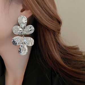 Macro shot of silver metal flower earrings with hammered texture on a model's ear