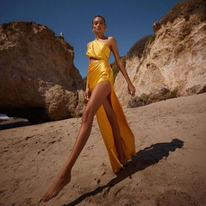Bright yellow one-shoulder satin dress with waist cutout and high side slit on beach
