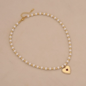 Detail of beaded pearl necklace with a gold heart pendant and deep red stone inlay