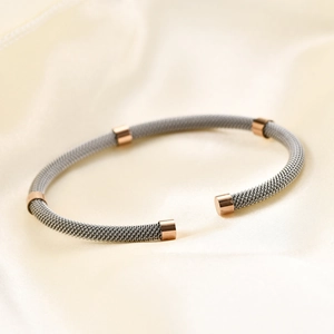 Braided stainless steel cable cuff bracelet with rose gold accents on silk background
