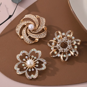 Détails de trois broches fleurs dorées avec perles et cristaux sur fond de cuir