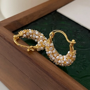 Macro detail of gold plated hoop earrings with inlaid white pearls and zircon crystals