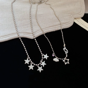 Detail of silver ball chain necklaces with hollow star and cloud charms on black background