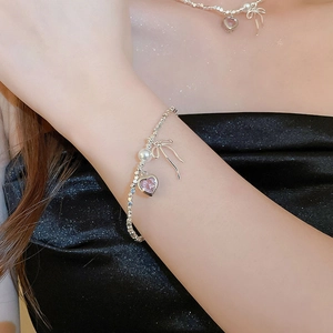 Detail of silver beaded bracelet with pink heart, bow charms and a pearl on model