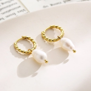 Macro detail of gold twisted hoop earrings featuring large baroque style white pearls