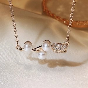 Elegant gold necklace with three pearls and zircon leaf pendant on beige satin background
