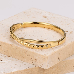 Elegant gold metal bangle with geometric serrated texture on stone display stand