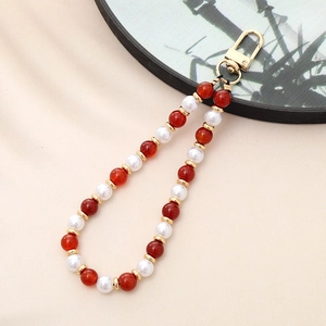 Detail of red agate and white pearl phone strap with elegant golden metal clasp