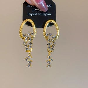 Detail of gold oval earrings with sparkling crystal tassels on black display card