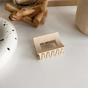 Detail of a square matte beige hair claw clip styled on a clean marble and wood surface