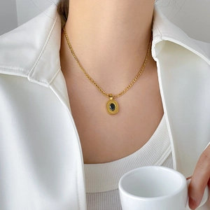 Close-up of a gold necklace with oval black gemstone pendant on a flat link chain