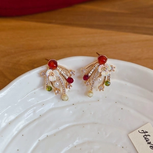 Macro shot of gold plated firework stud earrings with colorful crystals on a white ceramic tray